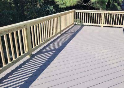 Long gray composite deck with pressure-treated wood railing casting shadows across the boards