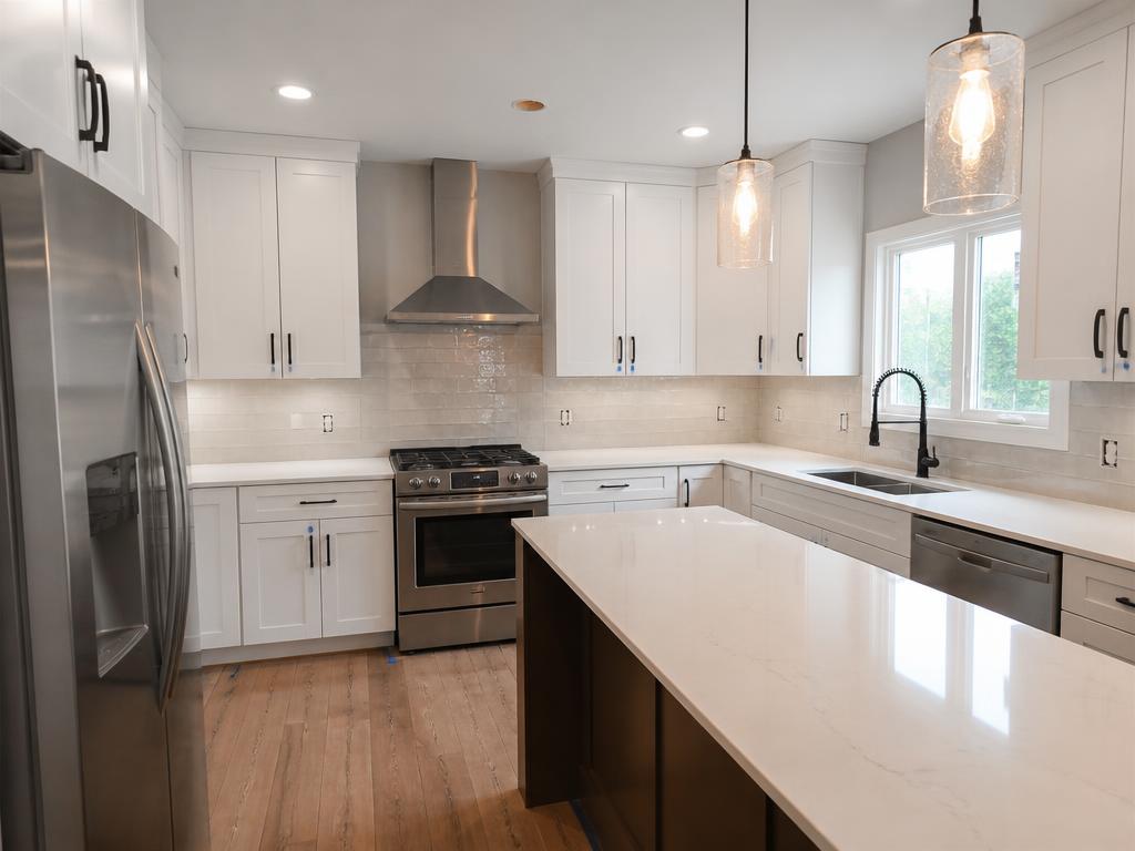 Completed kitchen remodel with white shaker cabinets, quartz island, and stainless appliances