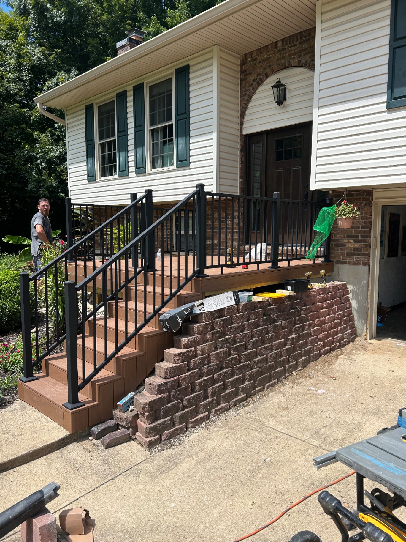 Front porch rebuilt with brown composite decking, black railing and a stone block retaining wall