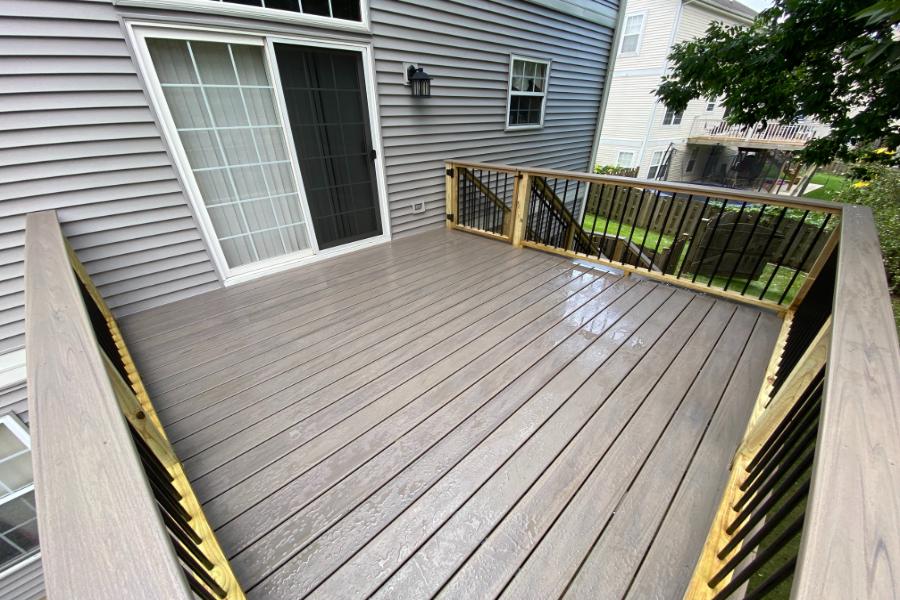 Gray composite backyard deck off a sliding glass door with cedar posts and black balusters