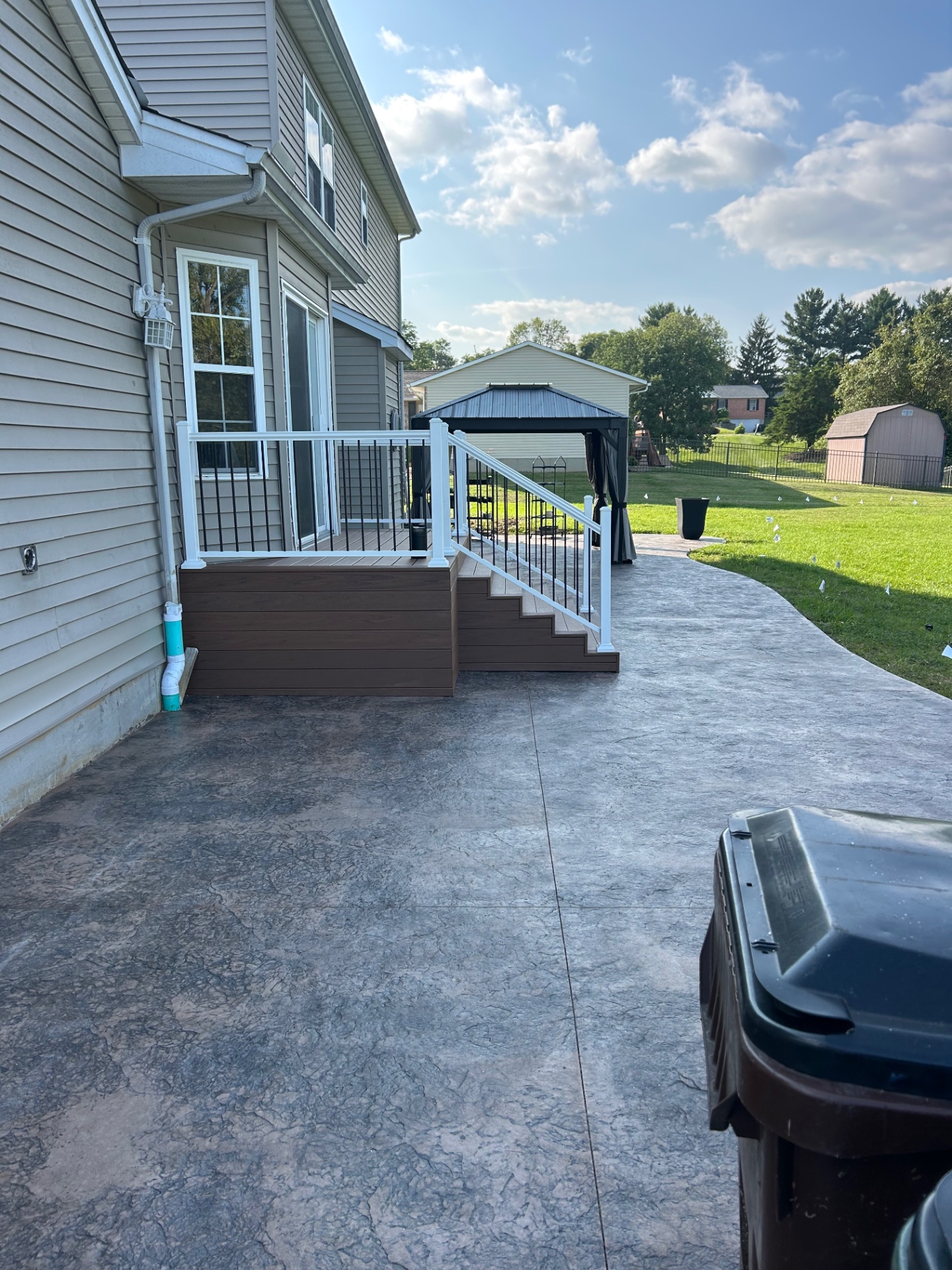 Composite deck with white railing and black balusters beside a stamped concrete patio
